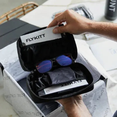 Person opening a FlyKitt travel pouch containing supplements and blue-lens glasses.